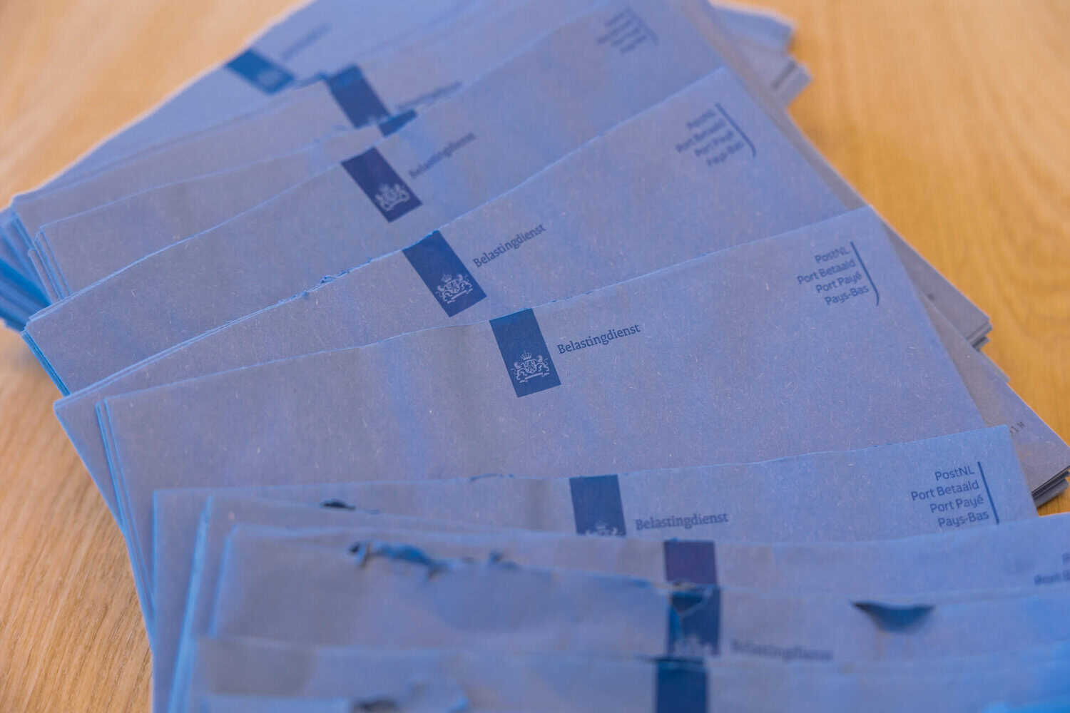 Stapel blauwe brieven van de belastingdienst op een houten tafel.